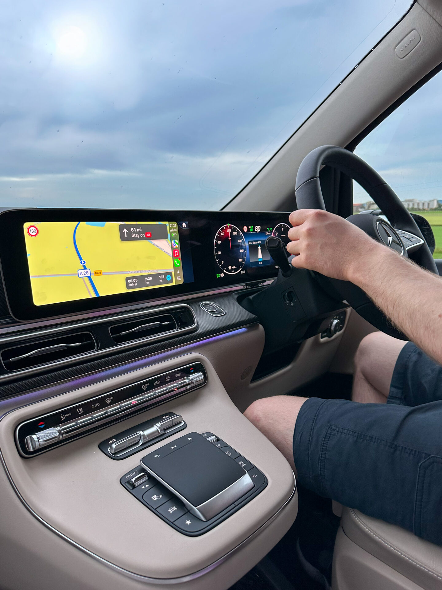 Photo of the front window & display panel of a WAV (Wheelchair Accessible Vehicle). The view through the window shows an overcast sky with the sun faintly shinning through the cloud cover. A GPS on the WAV's display panel shows the intended destination.