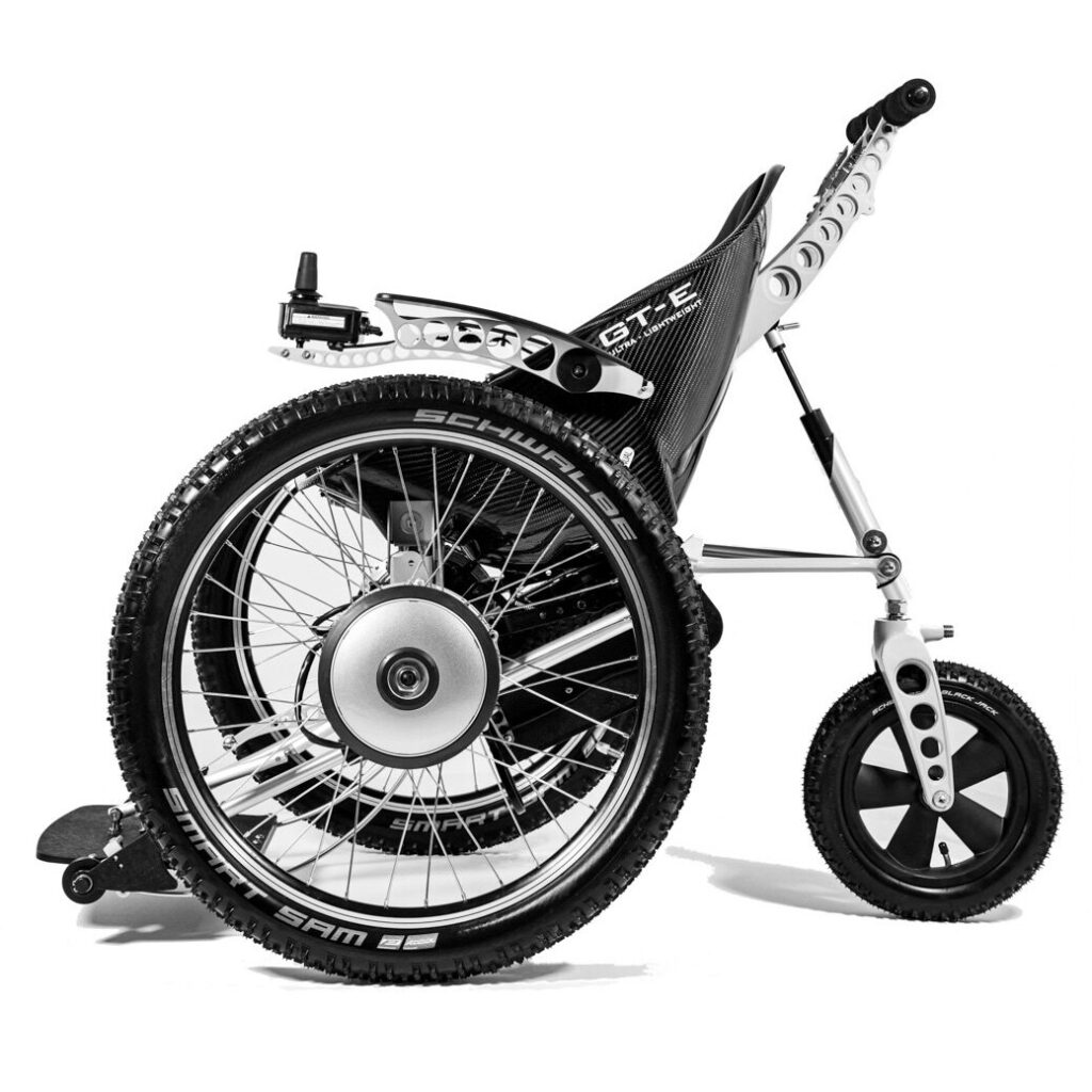 Side profile image of a 'Trikinetic GTE' manual & electric bespoke wheelchair with the unique ergonomically moulded carbon fibre seat, pair of massive 24 inch front wheels, & large rear wheel.