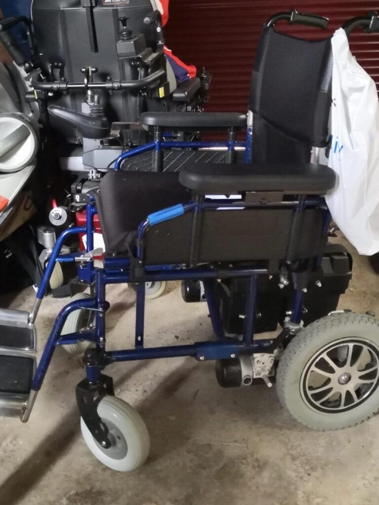 Side profile photo of a 'Betterlife Aries' electric wheelchair. The wheelchair is notable for its unusually large front castors, and small rear wheels.