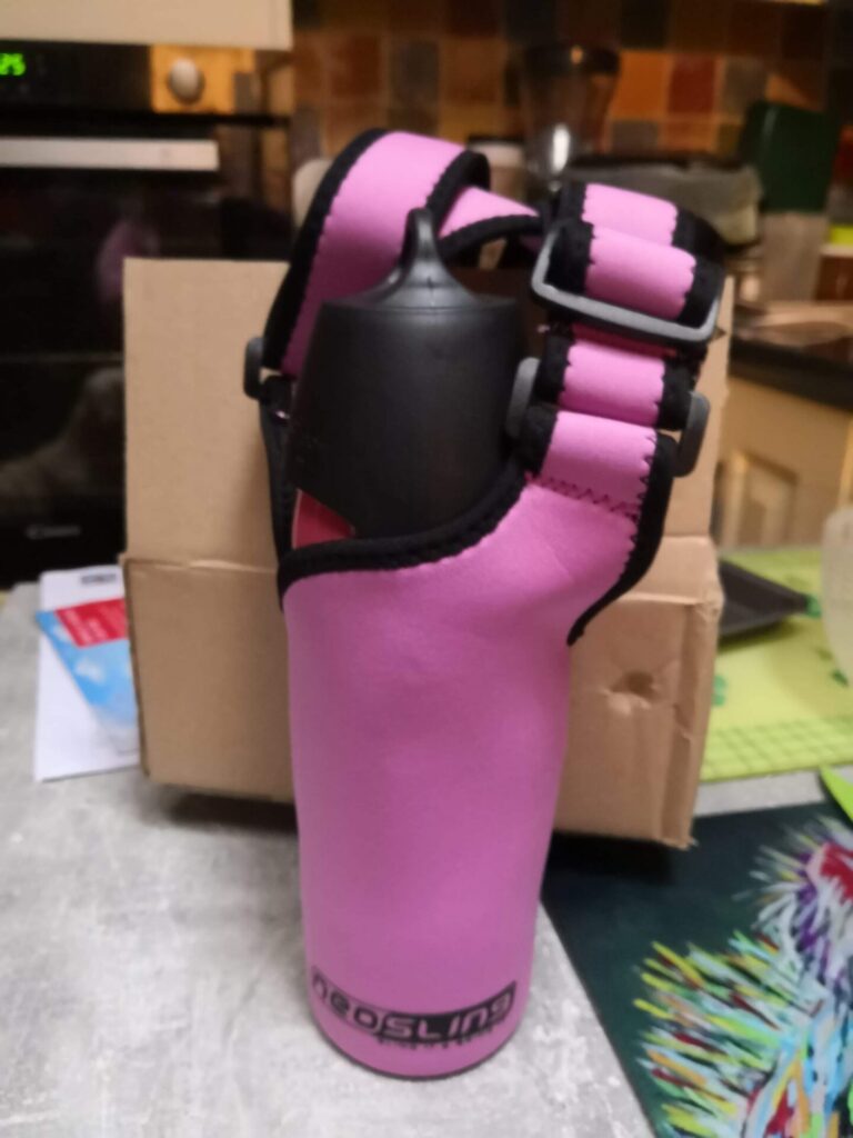 Photo of a pink 'Neoprene' thermo water bottle and lid held within a purple pink 'Neosling' water bottle carrier, allowing the bottle to be easily carried on a wheelchair.