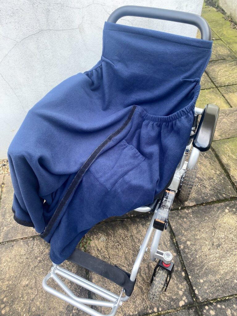 Photo of a blue 'NiCosy Wheelchair Blanket' opened up on a wheelchair to show its full size when not being used.