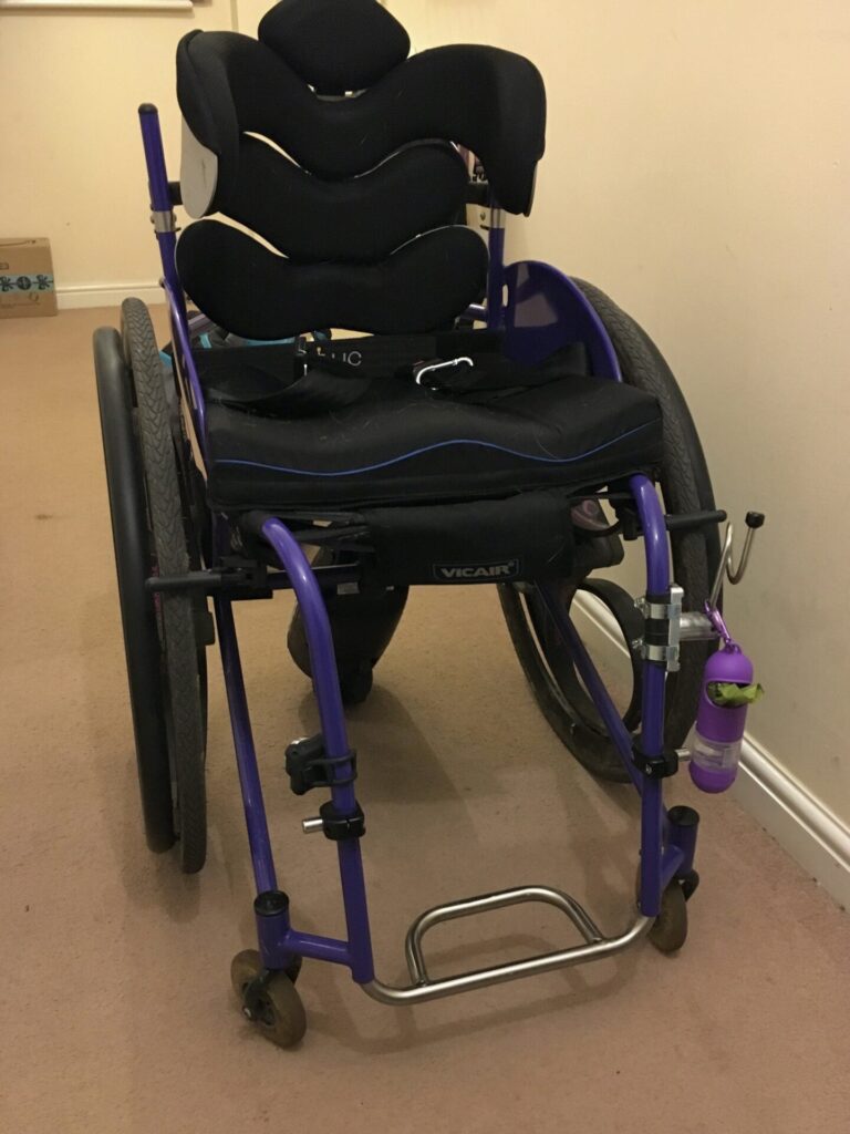 Photo of a 'RGK Maxlite' wheelchair with a 'Tartara backrest', and 'Vicair' seat cushion installed onto the seat of the wheelchair, & a 'SmartDrive' power assist unit installed on the rear end of the wheelchair.