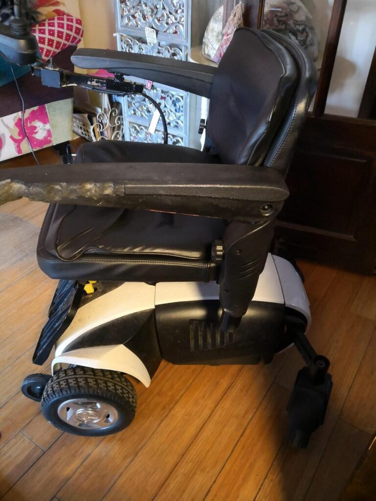 Side view profile photo of a 'Travelux Venture' riser electric wheelchair. Ware on the side of the left arm indicates that this wheelchair has been used extensively.