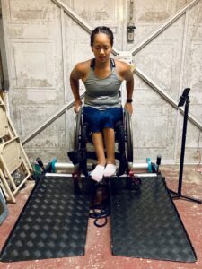 Photo of a woman using a wheelchair and an 'Invictus Active Trainer' treadmill- for wheelchair users, in the middle of a workout.