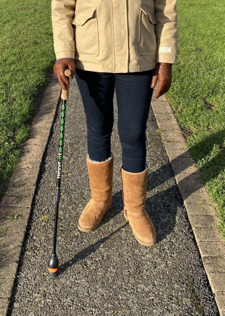 Photo of a person using a walking stick with a 'Flexyfoot Ferrule' attached to the bottom, going for a walk on the footpath in a park.