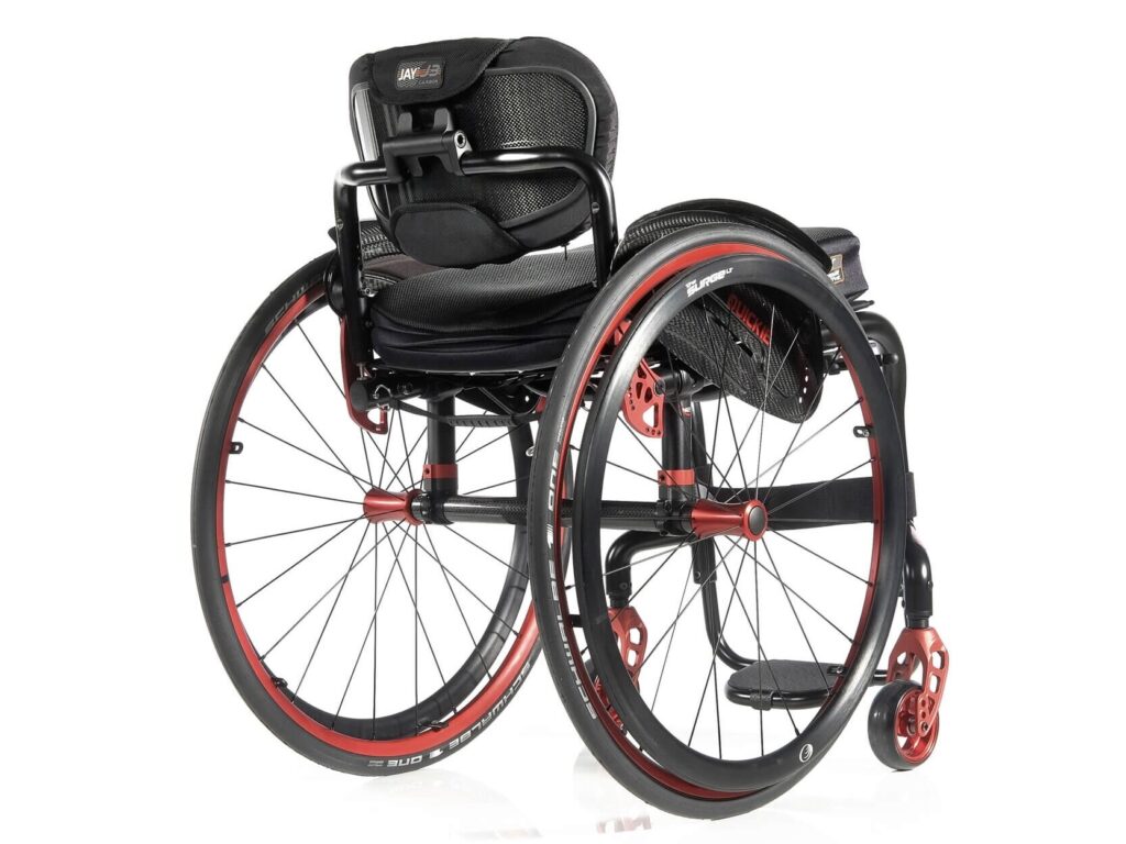 Three-quarter back profile image of a 'Quickie Helium' self-propelling rigid wheelchair. Metallic orange highlights show off the main wheels, casters, & important fixings on the wheelchair frame.
