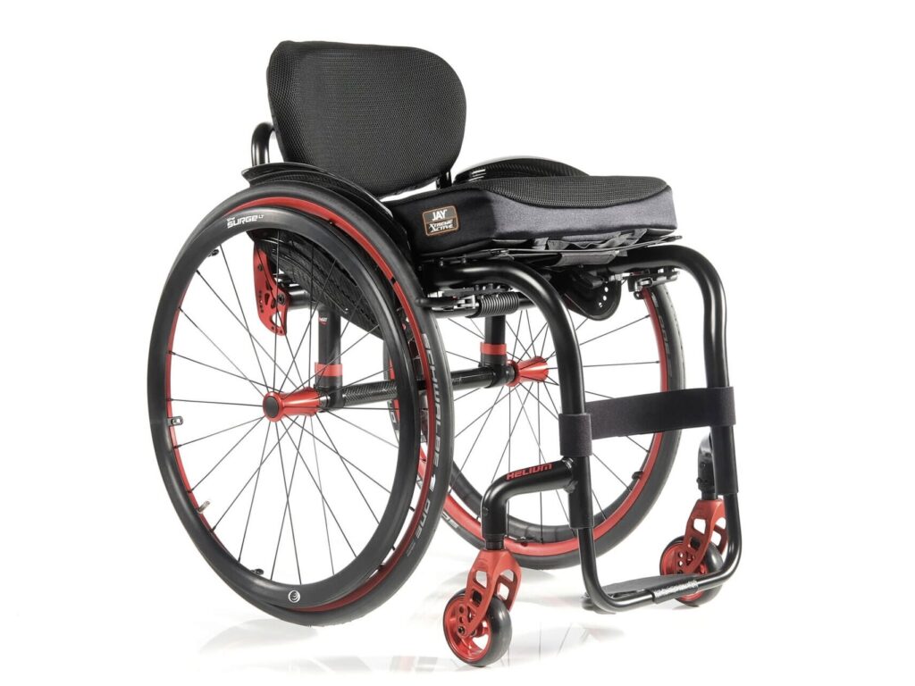 Three-quarter profile image of a 'Quickie Helium' self-propelling rigid wheelchair. Metallic orange highlights show off the main wheels, casters, & important fixings on the wheelchair frame.