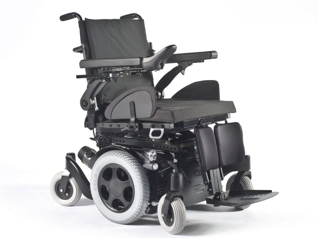 Side profile image of a 'Quickie Salsa M2' electric wheelchair, with a pair of castor wheels at both the front & the back of the chair and a set of wheels in the centre.
